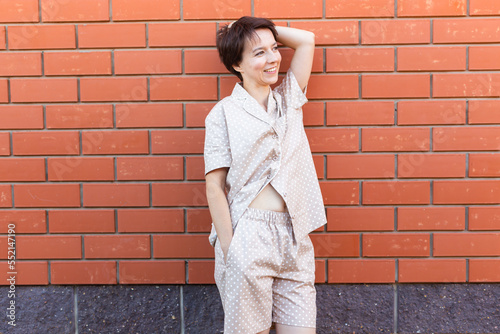 Cheerful woman in home wear pajama outdoor brick wall background emotions copy space and empty place for text - sleepwear and homewear concept