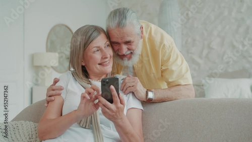 Elderly couple use smartphone relaxing together on sofa at home smiling feel happy. Have fun enjoy mobile application and watch video on internet. Modern gadget. Communication. Close up