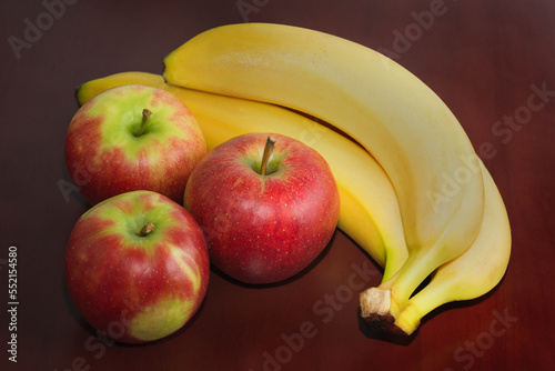 Three bananas and three apples on dark wooden background. Close up.