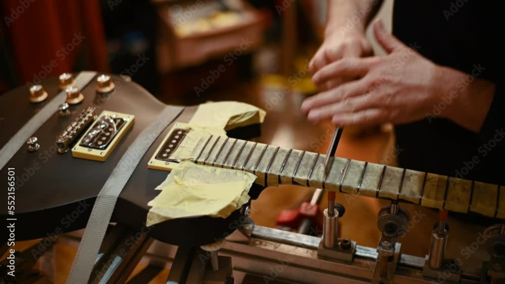 Luthier hands polishing the frets on the fretboard of the black