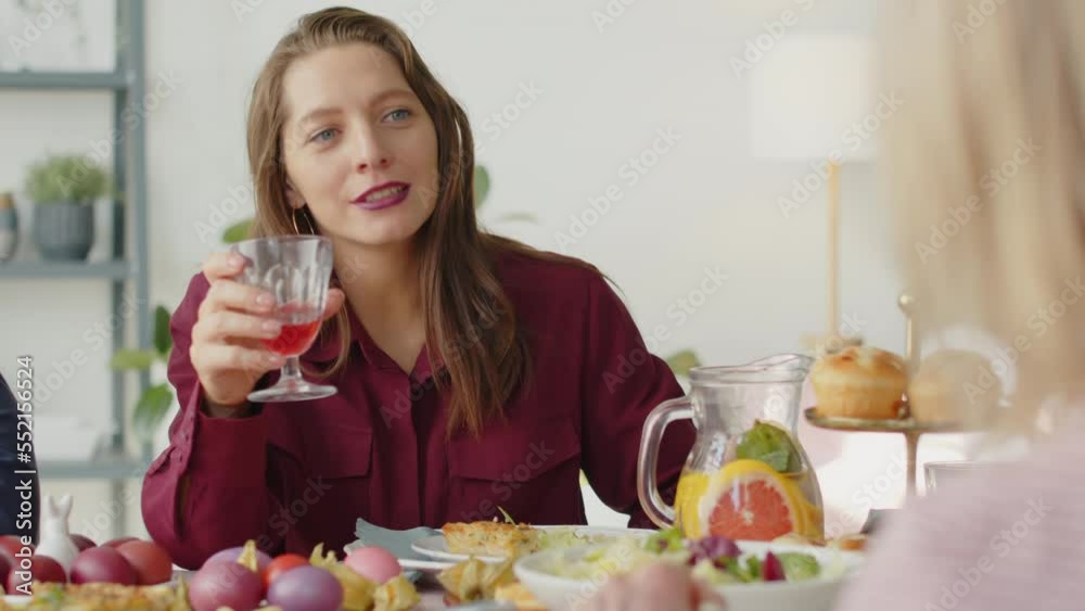 Over the shoulder shot of beautiful woman holding drink and chatting with family at dinner table while celebrating Easter together at home Over the shoulder shot of beautiful woman holding drink and chatting with family at dinner table while celebrating Easter together at home