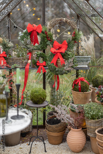 Glasshouse decorated with wreaths and red bows for a winter holidays at backyard. Concept of festive decorations for New Year holiday