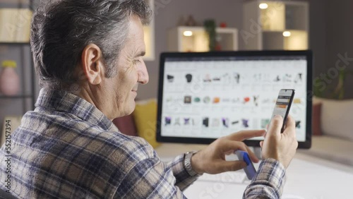 A man browsing and researching online shopping sites to buy new products.
The man is shopping online from his home computer and phone.
