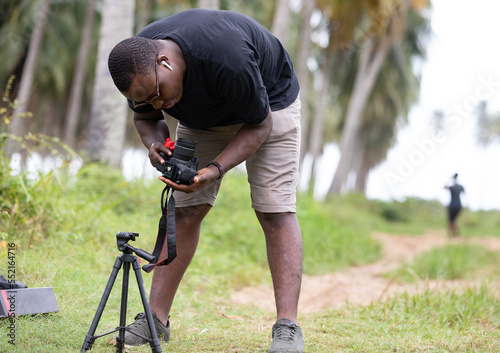 Portrait of a young black African photographer unpacking his photography equipment, a tripod, in a West African village during an outdoor photo shoot