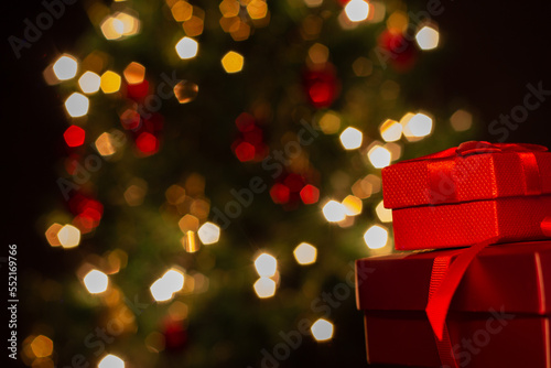 Duas caixas de presente, vermelhas, com um laço de fita, com uma árvore de Natal ao fundo. photo