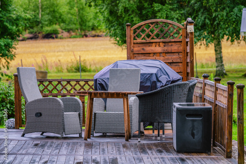 Heavy rain at wooden terrace with summer chairs, wooden table, grill covered against of rain. Blurry green forest at background. Everything is very wet. Countryside, day time. close up photo