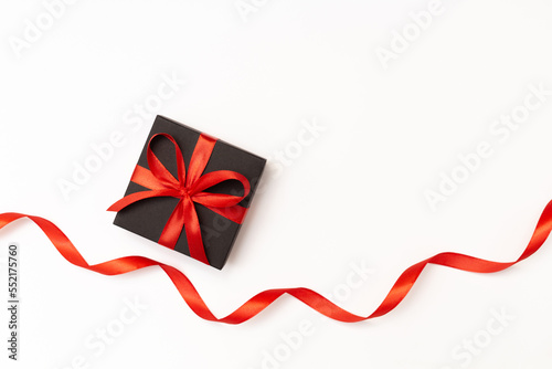 Flat lay of black present box with red bow and ribbon on the white background