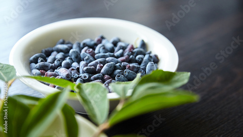 Fresh honeyberry (Lonicera caerulea) in white bowl on wooden table. Blue haskap berry with green leaves photo