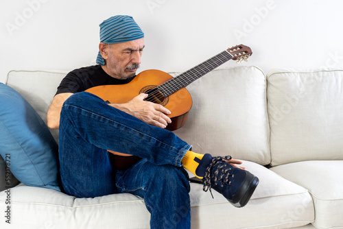 Old Man Practicing to Play Guitar Sitting on Sofa at Home © klenger
