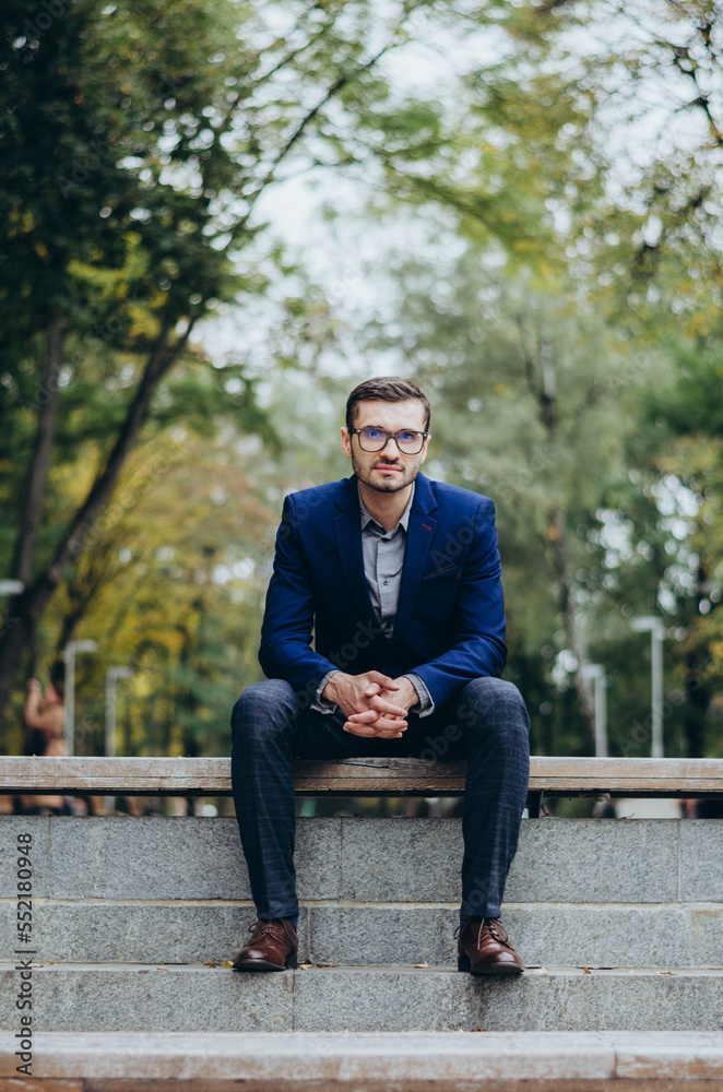 Obraz premium A man in a suit is sitting on a bench in the park