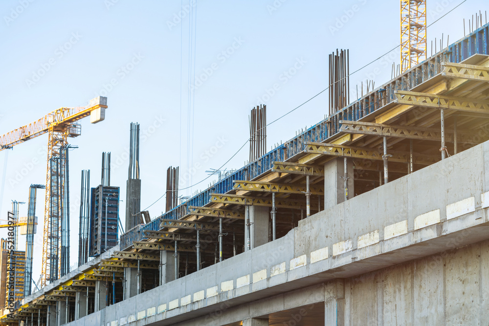 Construction site with monolithic concrete yellow and gray frame scaffolding and yellow construction tower cranes on the background. With lens flare, Construction concept.