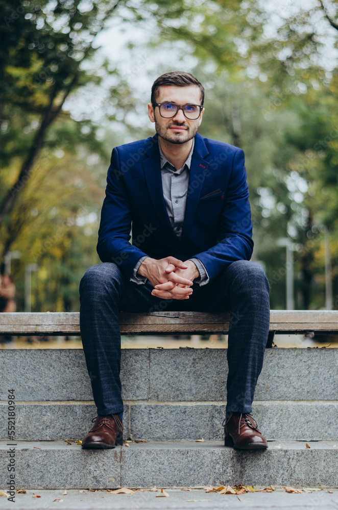 Obraz premium A man in a suit is sitting on a bench in the park