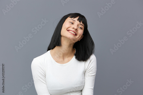 a happy woman stands on a dark background in a tight white T-shirt, slightly tilted her head back, calmly lowering her hands down