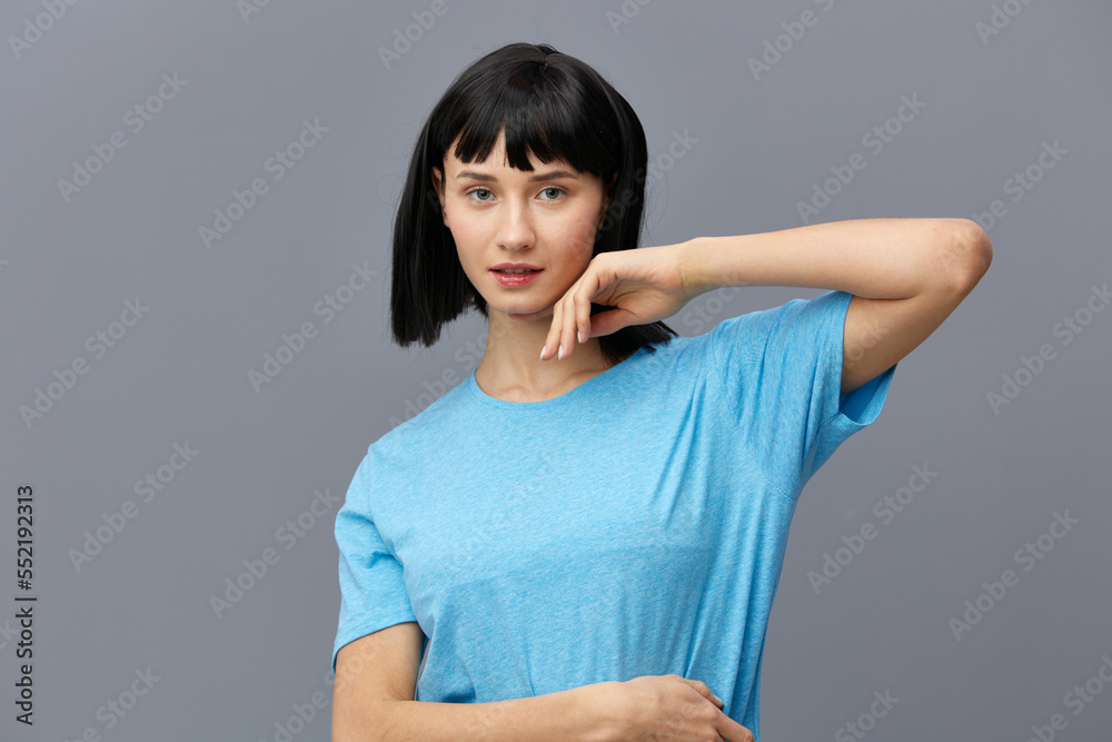 a peaceful woman stands on a dark background in a blue T-shirt, raised her elbow up, leaning her fingers against her face, putting the second fart on her stomach a peaceful woman stands on a dark background in a blue T-shirt, raised her elbow up, leaning her fingers against her face, putting the second fart on her stomach