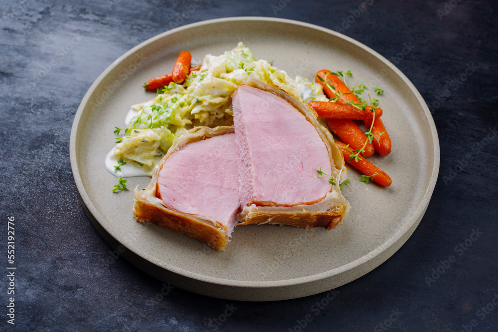 Gebackenes Kasseler Schweinesteak im Teigmantel mit Wirsing Kohl und Baby Karotten serviert als close-up auf einem Design Teller mit Textfreiraum Gebackenes Kasseler Schweinesteak im Teigmantel mit Wirsing Kohl und Baby Karotten serviert als close-up auf einem Design Teller mit Textfreiraum