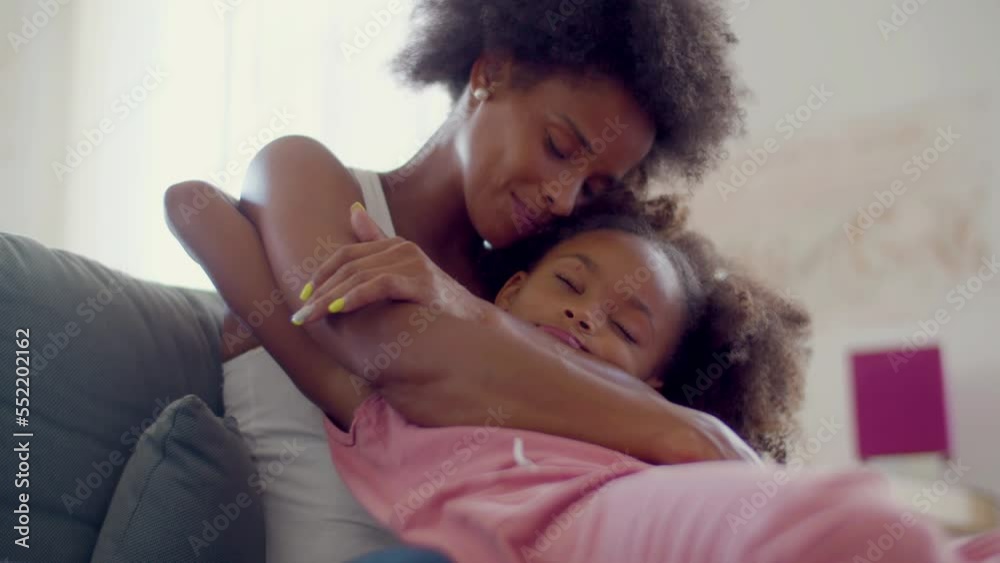 Closeup of cute Black girl sitting on mums lap while hugging each other and enjoying time together. Loving African American woman showing affection to her child. Motherhood, happy family concept.