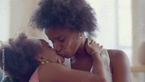 Closeup of loving mother and cute little daughter hugging and kissing. Beautiful African American woman showing affection holding and caressing her child. Static shot. Motherhood, happy family concept photo