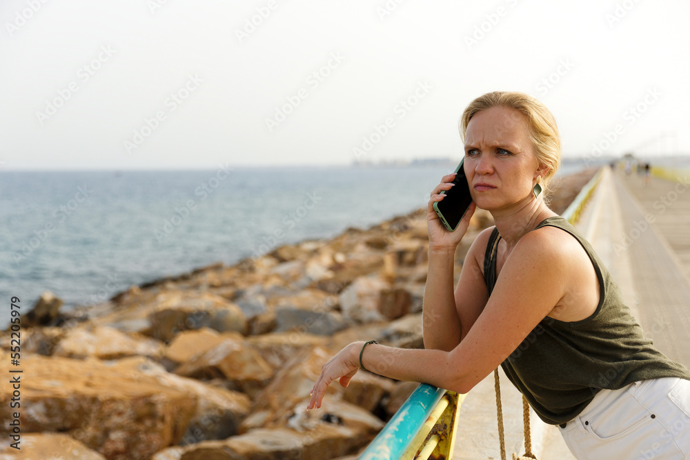A young stylish woman communicates on a smartphone on the city embankment, Rest and work in nature, by the sea