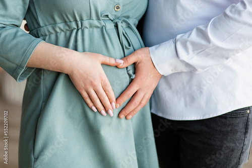 A pregnant woman and a loving husband hugs her stomach on a white background. The feeling of the baby s movement by a couple on the pregnant woman s stomach. Close-up.