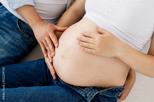 A pregnant woman and a loving husband hugs her stomach on a white background. The feeling of the baby's movement by a couple on the pregnant woman's stomach. Close-up.