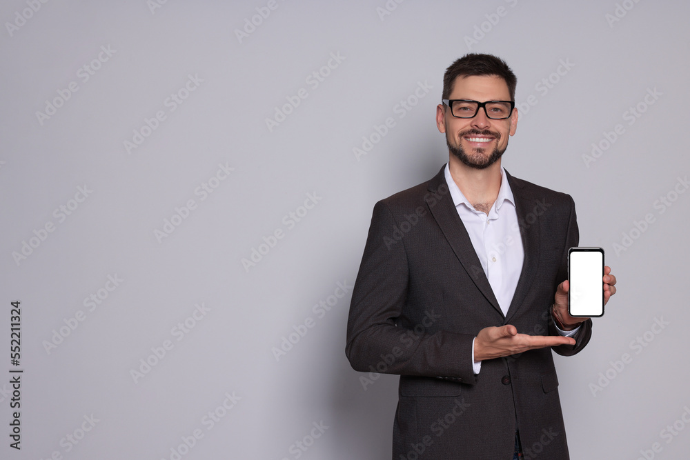 Smiling man in suit showing smartphone on light grey background. Space for text Smiling man in suit showing smartphone on light grey background. Space for text