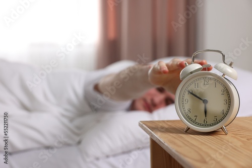 Man turning off alarm clock in bedroom, focus on hand. Space for text