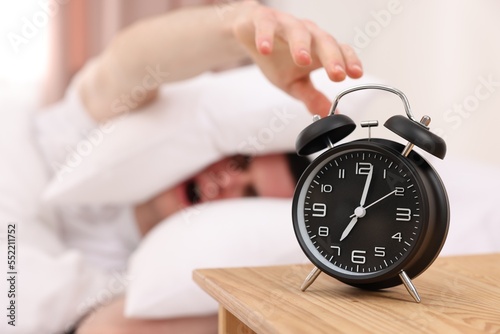 Yawning man turning off alarm clock in bedroom, focus on hand. Space for text