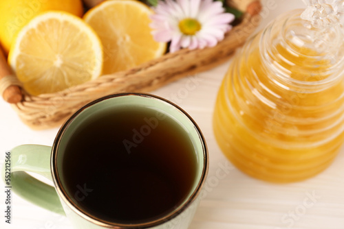 Mug with delicious tea and honey on white table, closeup
