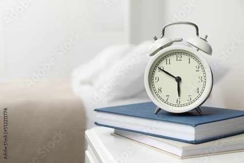 Alarm clock and books on white nightstand in bedroom, space for text