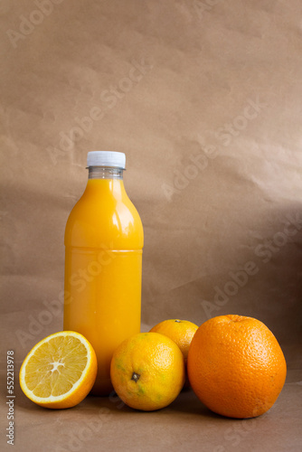 still life - a plastic bottle with orange juice and three ripe fruits and a cut off half of an orange - close-up