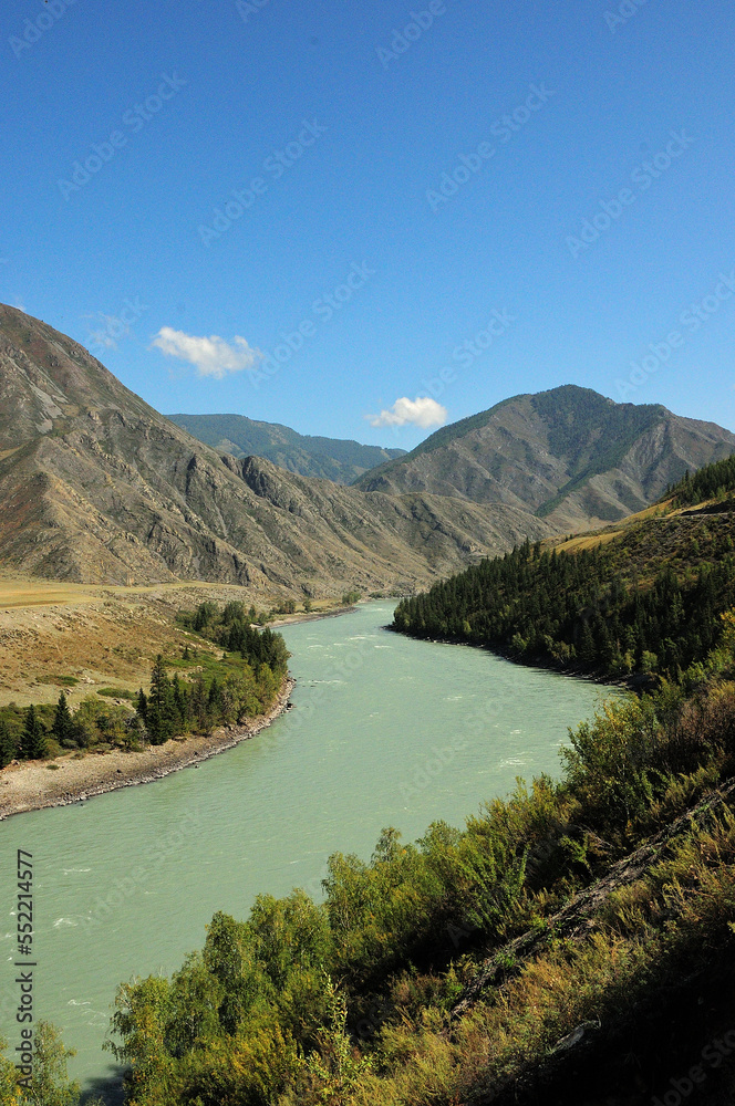 The winding bed of a beautiful river flowing through a picturesque mountain valley on a warm autumn day.