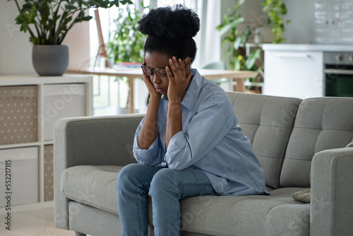 Discouraged sad African woman sits on sofa and feeling stressed because of loneliness. Unhappy depressed black girl suffering from depression after breaking up with boyfriend or death of loved one 