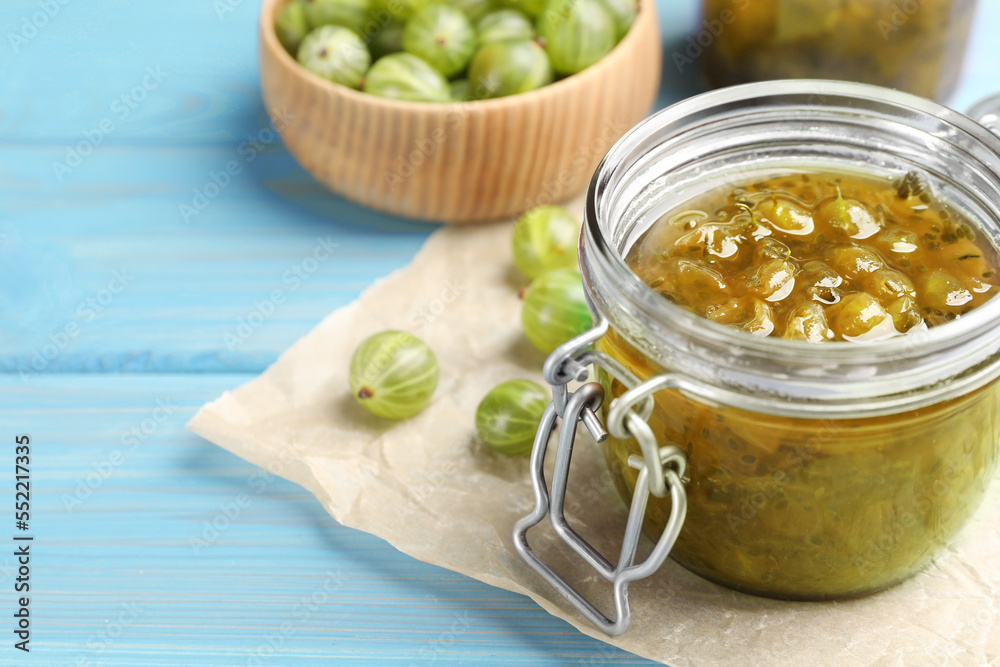 Jar of delicious gooseberry jam and fresh berries on blue wooden table, closeup. Space for text Jar of delicious gooseberry jam and fresh berries on blue wooden table, closeup. Space for text