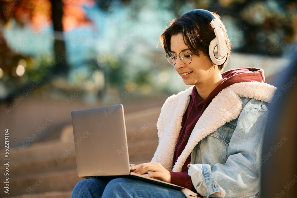 Young woman with headphones using laptop outdoors. Young woman with headphones using laptop outdoors.