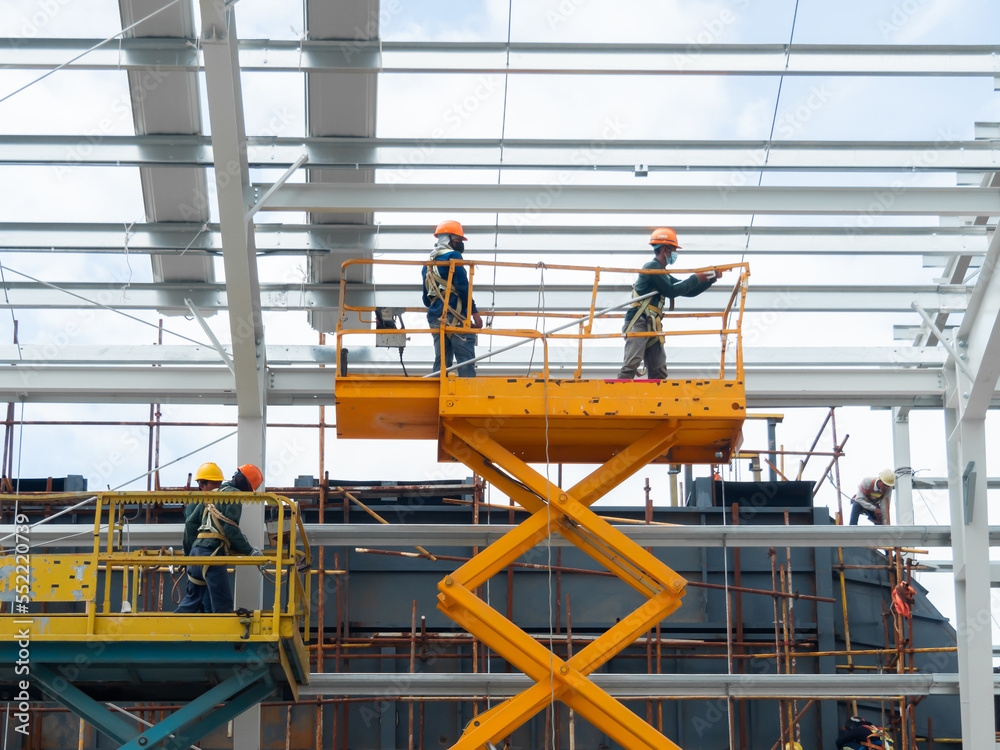 Workers install lighting fixture in a hug industrial warehouse using hydraulic scissor lift. MEP work in construction site. Workers install lighting fixture in a hug industrial warehouse using hydraulic scissor lift. MEP work in construction site.