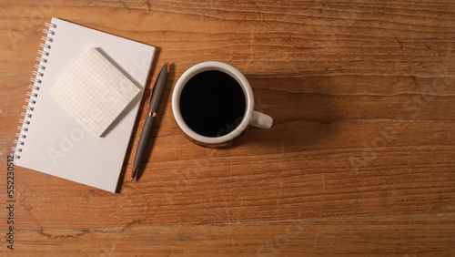 Top view of cup of coffee  sticky note  notebook and pen on wooden table. Copy space for your text.
