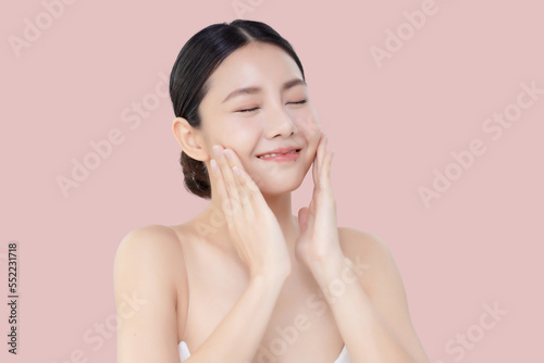 Studio shot Beautiful young Asian woman with clean fresh skin massage her face isolated on pink background.