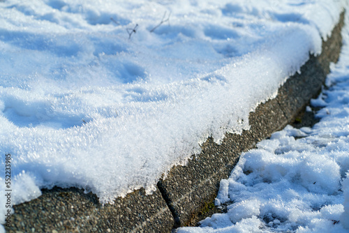Frosty snow on cement curb in sunlight