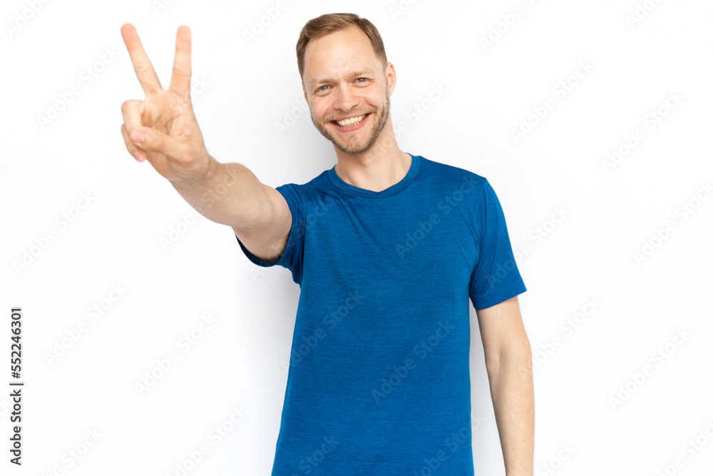 Happy White man showing peace gesture at camera. Portrait of smiling guy looking at camera and standing on white background. Satisfaction, achievement, winning concept Happy White man showing peace gesture at camera. Portrait of smiling guy looking at camera and standing on white background. Satisfaction, achievement, winning concept