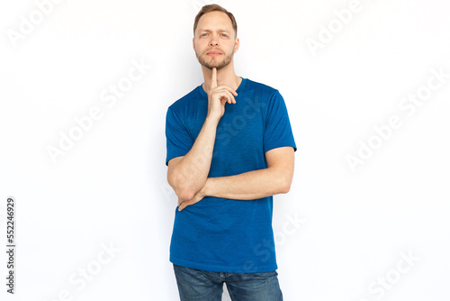 Pensive man looking at camera, touching chin with finger. Peaceful man in T-shirt looking at camera while standing on white background. Imagination, wonder, inspiration concept