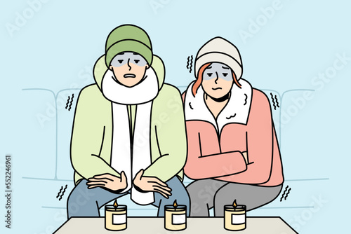 Man, woman in hats, puffer jackets are sitting, warming themselves near burning candles in unheated room. Boy, girl are cold at home in winter. People freeze. Vector contour line colored illustration.