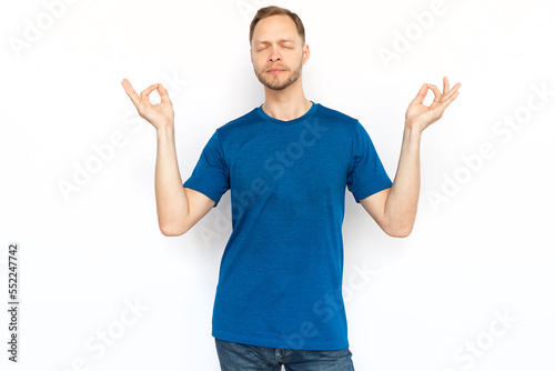 Relaxed man standing and showing zen gesture. Peaceful man standing in lotus position on white background, meditating with closed eyes and breathing. Yoga, relaxation concept