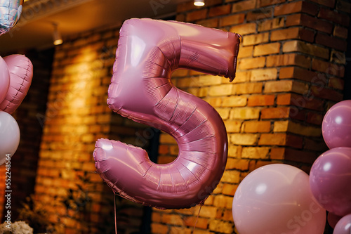Festive balloons in the form of the number five pink. Hanging on a rope near round balls.