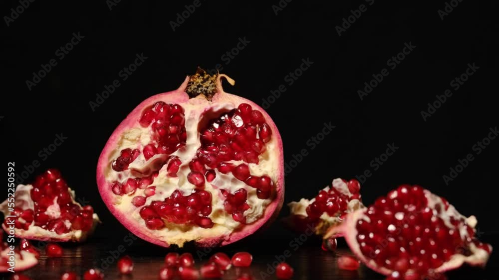 broken pomegranate with red ripe juicy kernels on the table on a black background