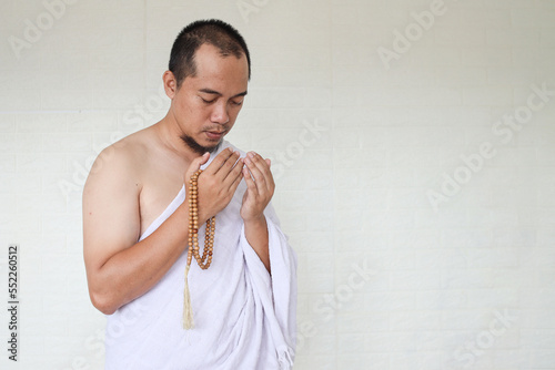 Asian muslim man wearing white ihram clothes and praying while holding prayer beads photo