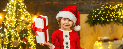 Happy cute child in Santa hat with present have a Christmas. Little Santa Claus gifting gift. © Volodymyr