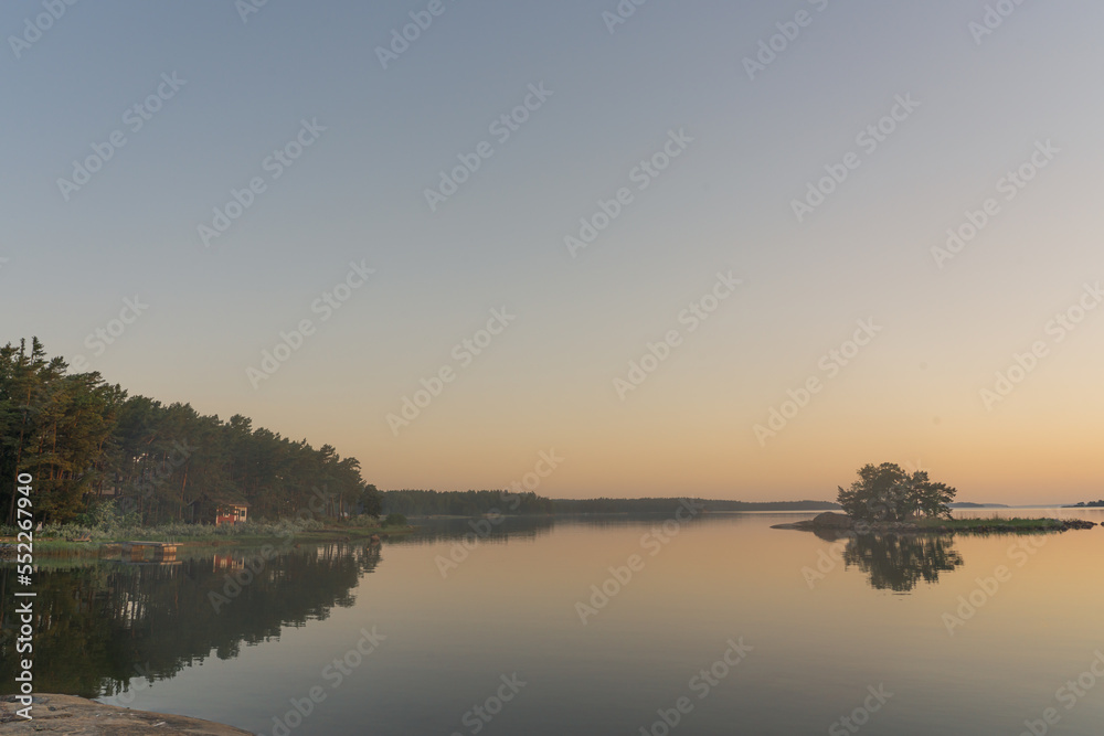 Nagu, Finland - 12.06.2022: The quiet shore of the bay after sunset. A line of trees and a small island on the horizon. Nature of Finland. Natural background. Space for text.