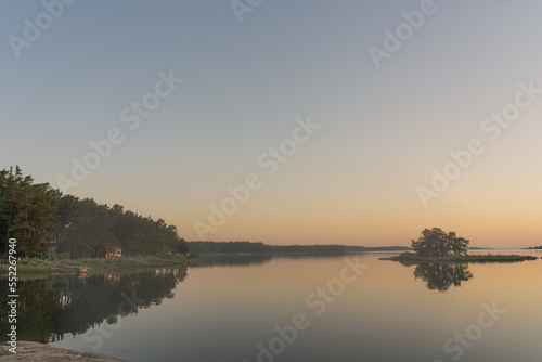 Nagu, Finland - 12.06.2022: The quiet shore of the bay after sunset. A line of trees and a small island on the horizon. Nature of Finland. Natural background. Space for text.