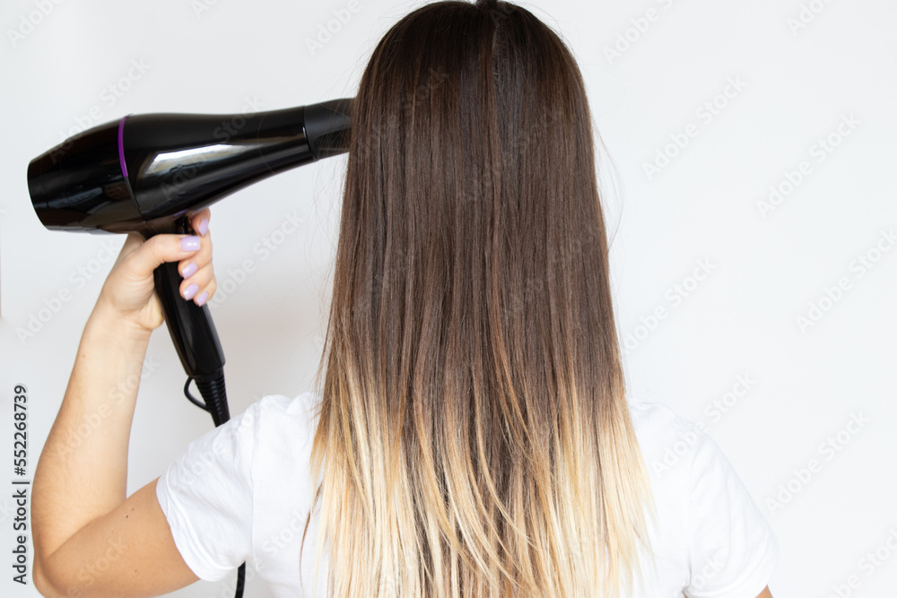 Fototapeta premium The girl dries her hair with a hairdryer on a white background, hair dryer and hair, hairdresser