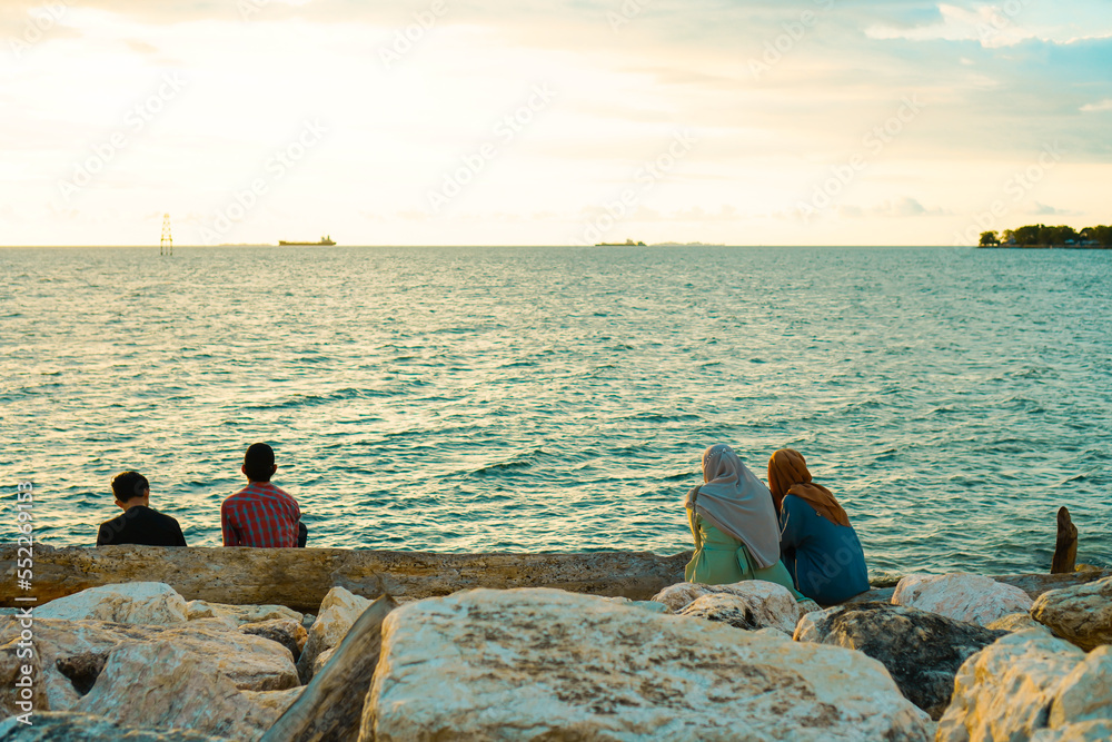 Rear view of friends enjoying the atmosphere sitting on the beach Rear view of friends enjoying the atmosphere sitting on the beach